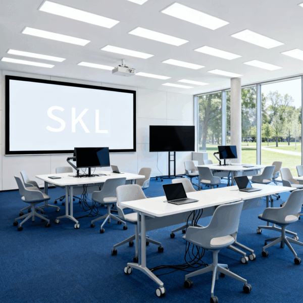 Das Bild zeigt eine modernen Schulungsraum, ausgestattet mit Laptops und digitalen Präsentationsmöglichkeiten. Auf dem digitalen Whiteboard steht in großen Lettern "SKL".
